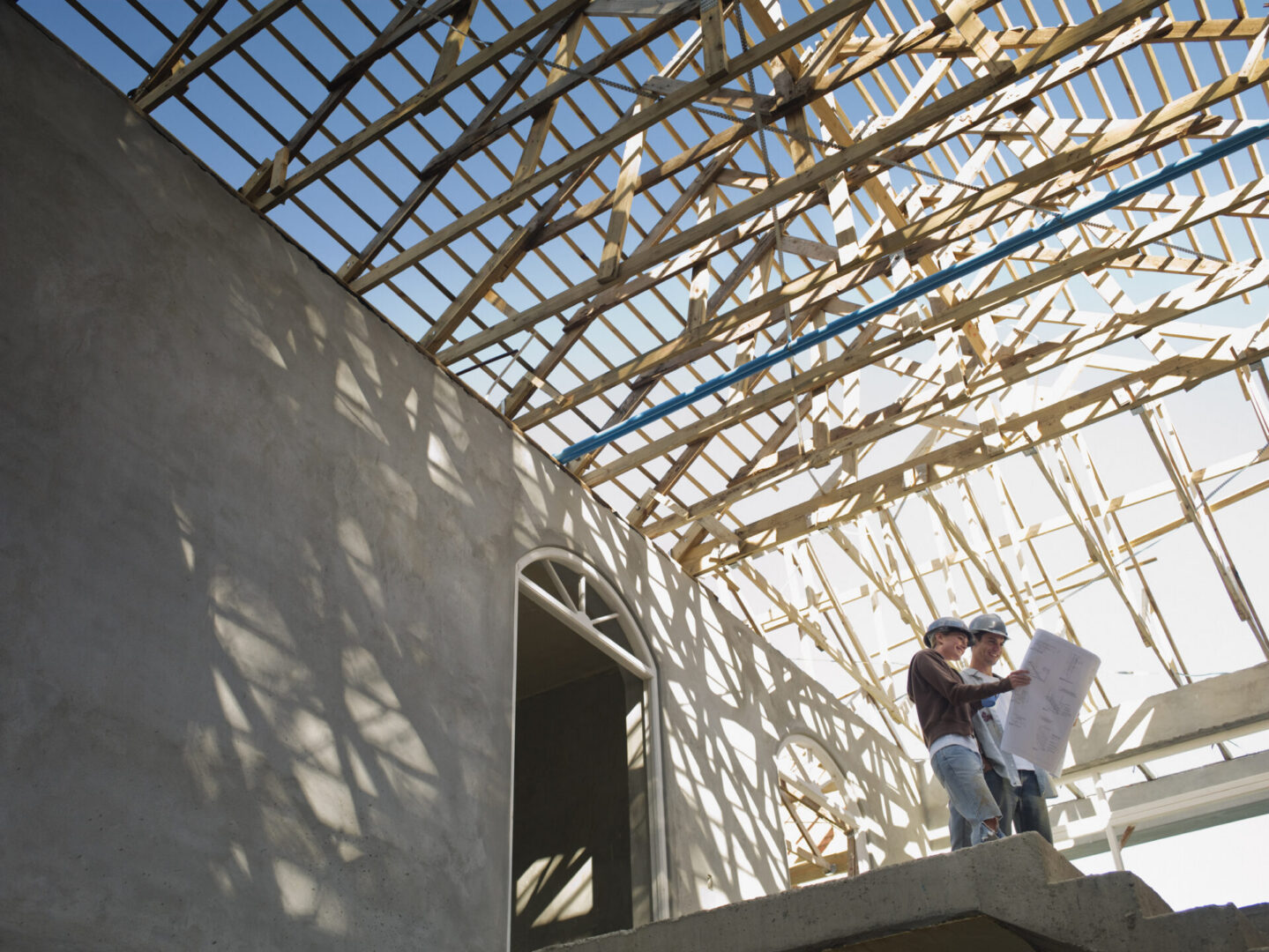 Construction workers examining blueprints under framework.